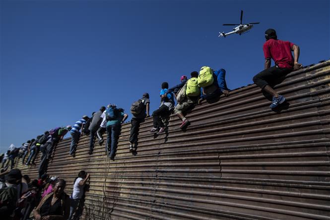 Người di cư trèo qua bức tường biên giới Mexico-Mỹ, gần cửa khẩu El Chaparral ở Tijuana, bang Baja California, Mexico. Ảnh: AFP/ TTXVN